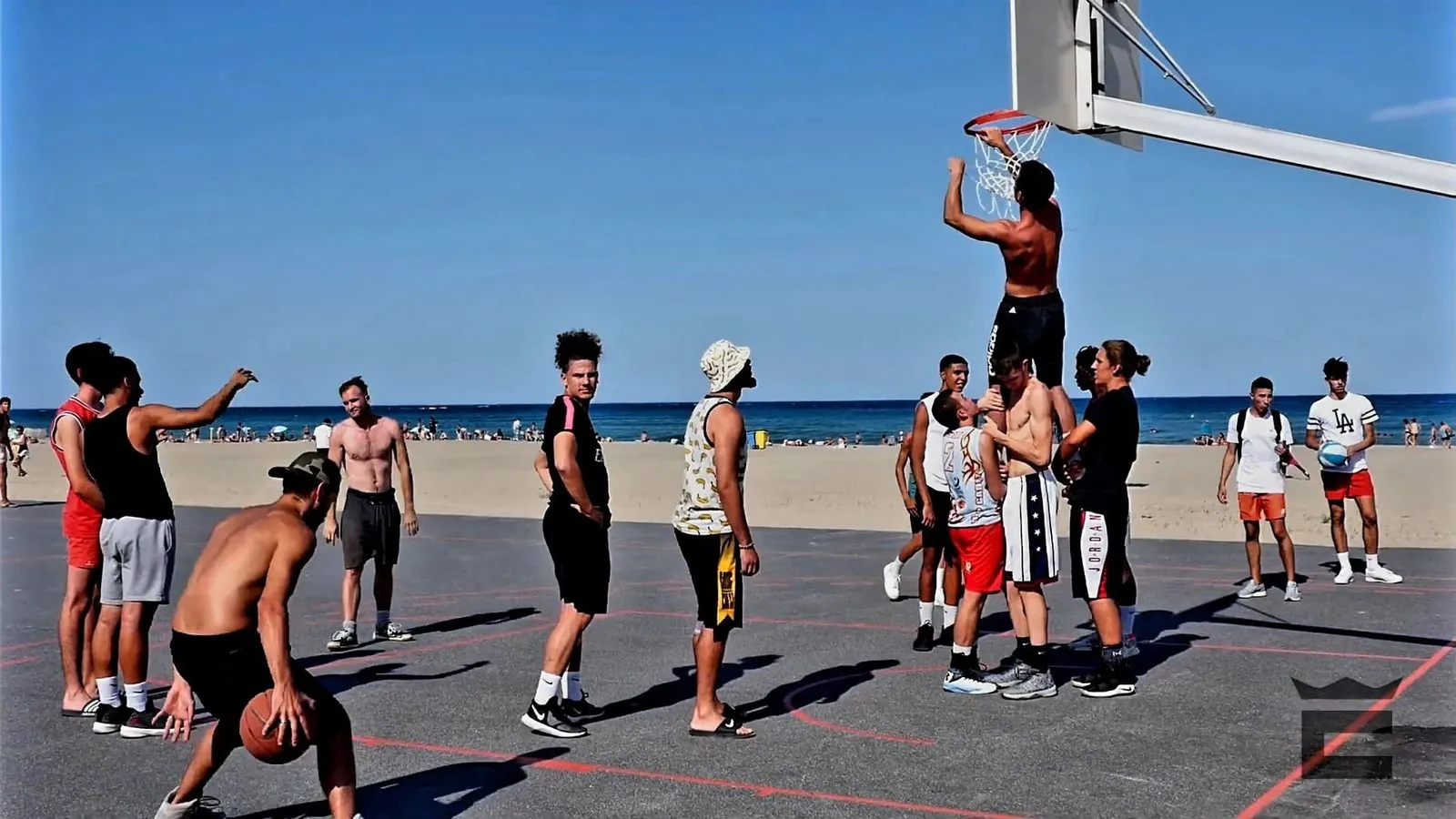 Un joueur accroché à l'arceau après un dunk, sur un playground en bord de mer, entouré des autres
